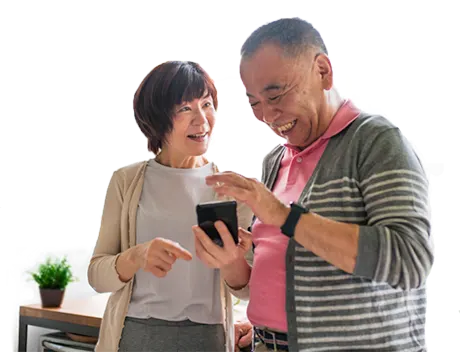 Two seniors stand side-by-side, smiling and looking at a mobile phone screen.